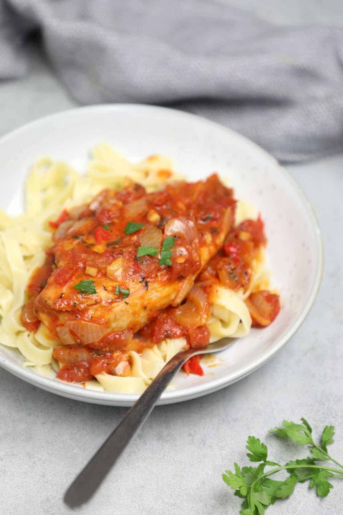 chicken in tomato sauce served on pasta and garnished with parsley.