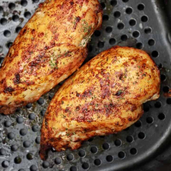 2 pieces cooked frozen chicken breasts in air fryer basket.