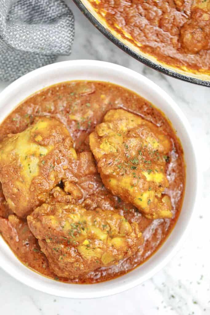 chicken thigh curry served on a white plate.