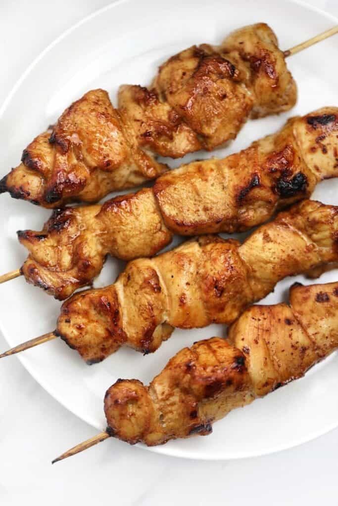 chicken on stick/ skewers displayed on a white plate.