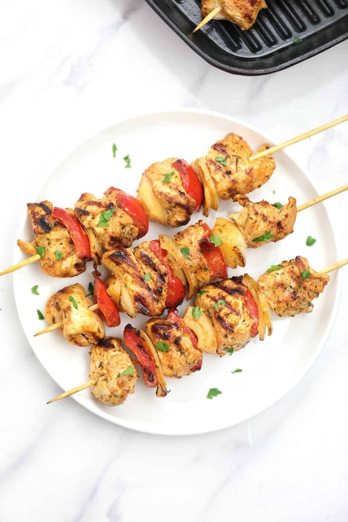 3 cooked chicken skewers on a white plate.