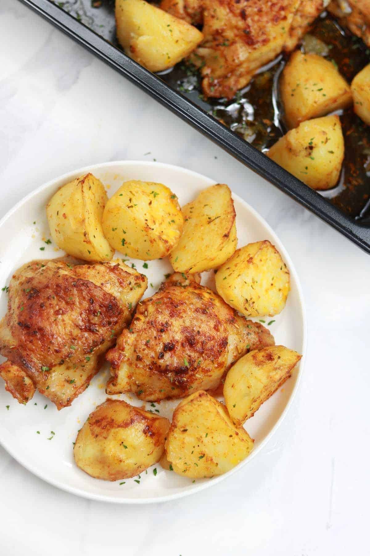 baked chicken and potatoes displayed on a plate and  baking pan.
