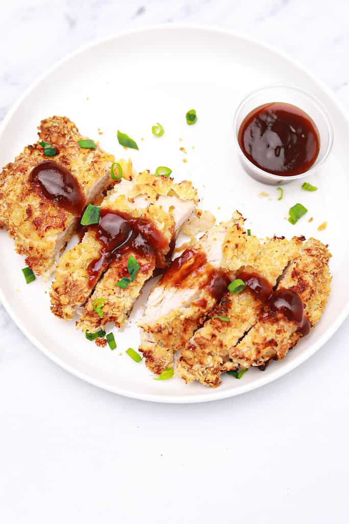 chicken katsu served on a white plate and garnished with spring onions.